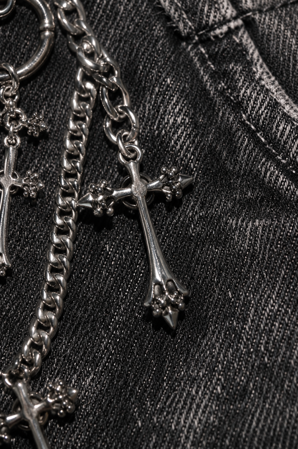 Macro detail of ADRN 01 Cross silver-tone metal chain on black denim