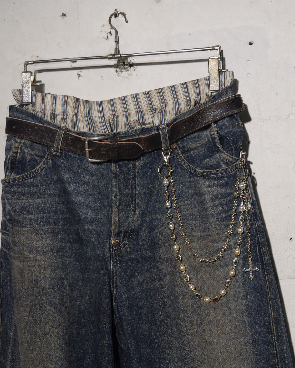 ADRN 02 Circle Gold pants chain attached to oversized washed blue jeans hanging against a raw wall
